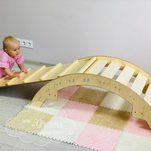 A baby playing on a two-in-one wooden climbing arch and rocker.